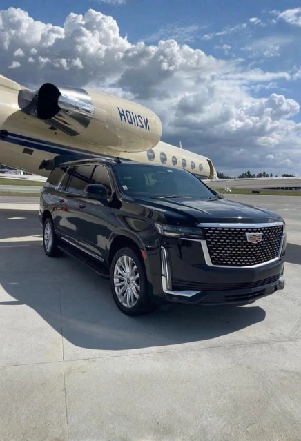 A luxury black cadillac escalade parked beside a plane