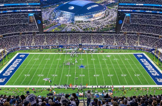 high angle view of a packed at&t stadium during a dallas cowboys game, showing the football field, players, and cheering fans.